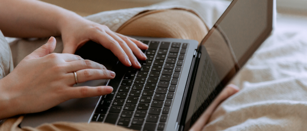 A woman types on an open laptop on a bed